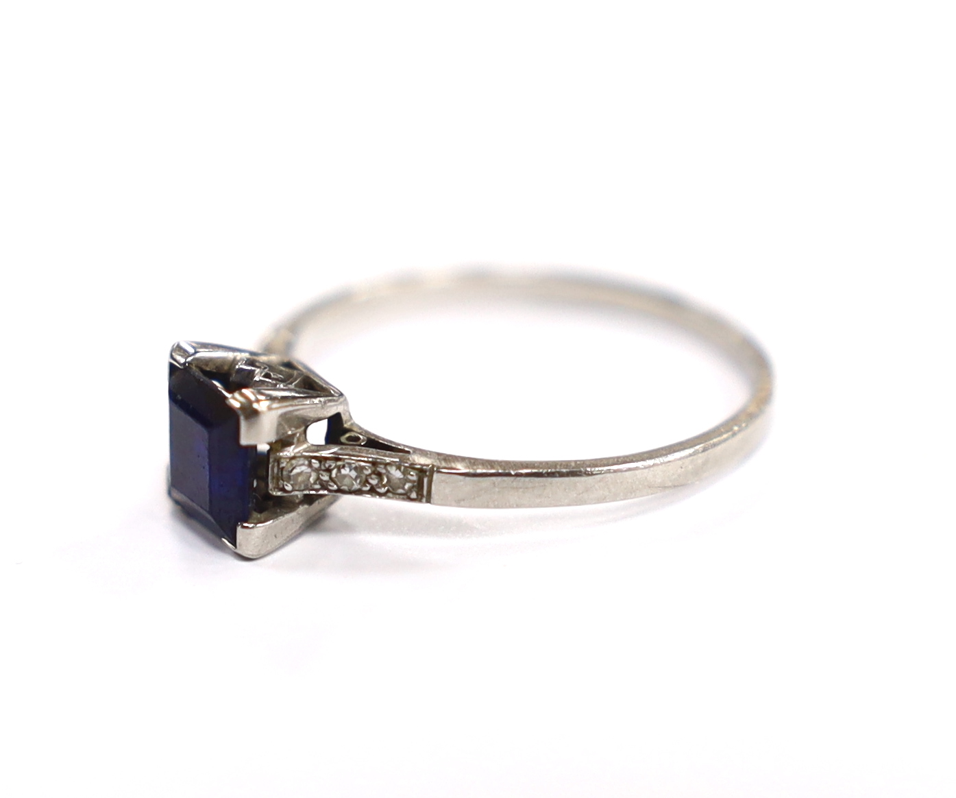 A white metal (stamped plat) and single stone square cut sapphire set ring, with diamond chip set shoulders, size P, gross weight 2.8 gram.